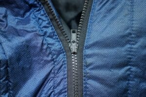Close-up of a black open-end plastic molded zipper on a blue jacket, ideal for jackets, hoodies, coats, sportswear, and professional tailoring projects.
