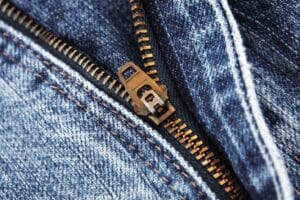Close-up of a premium antique brass metal jeans zipper on blue denim fabric for trousers, jackets, skirts, and professional tailoring projects.